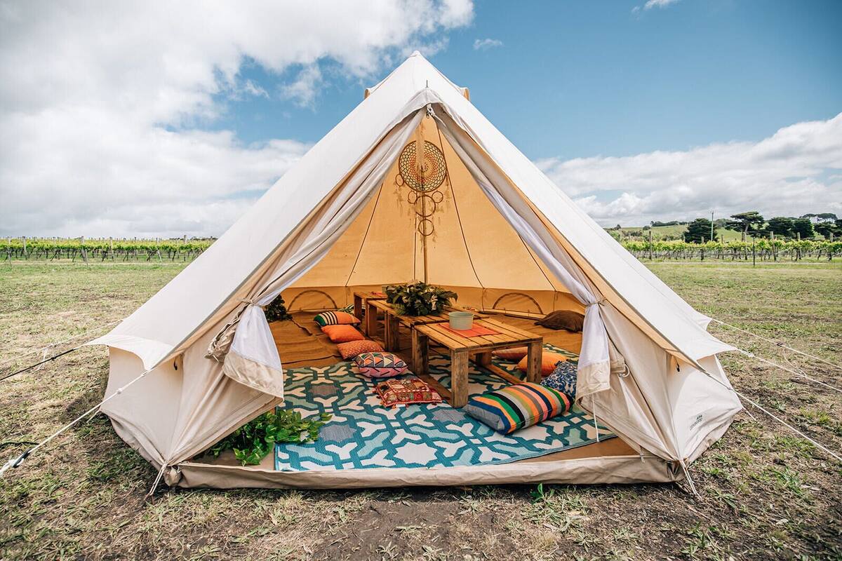 A geodesic dome tent with a table and cushions inside, set on a patterned rug in an open field.