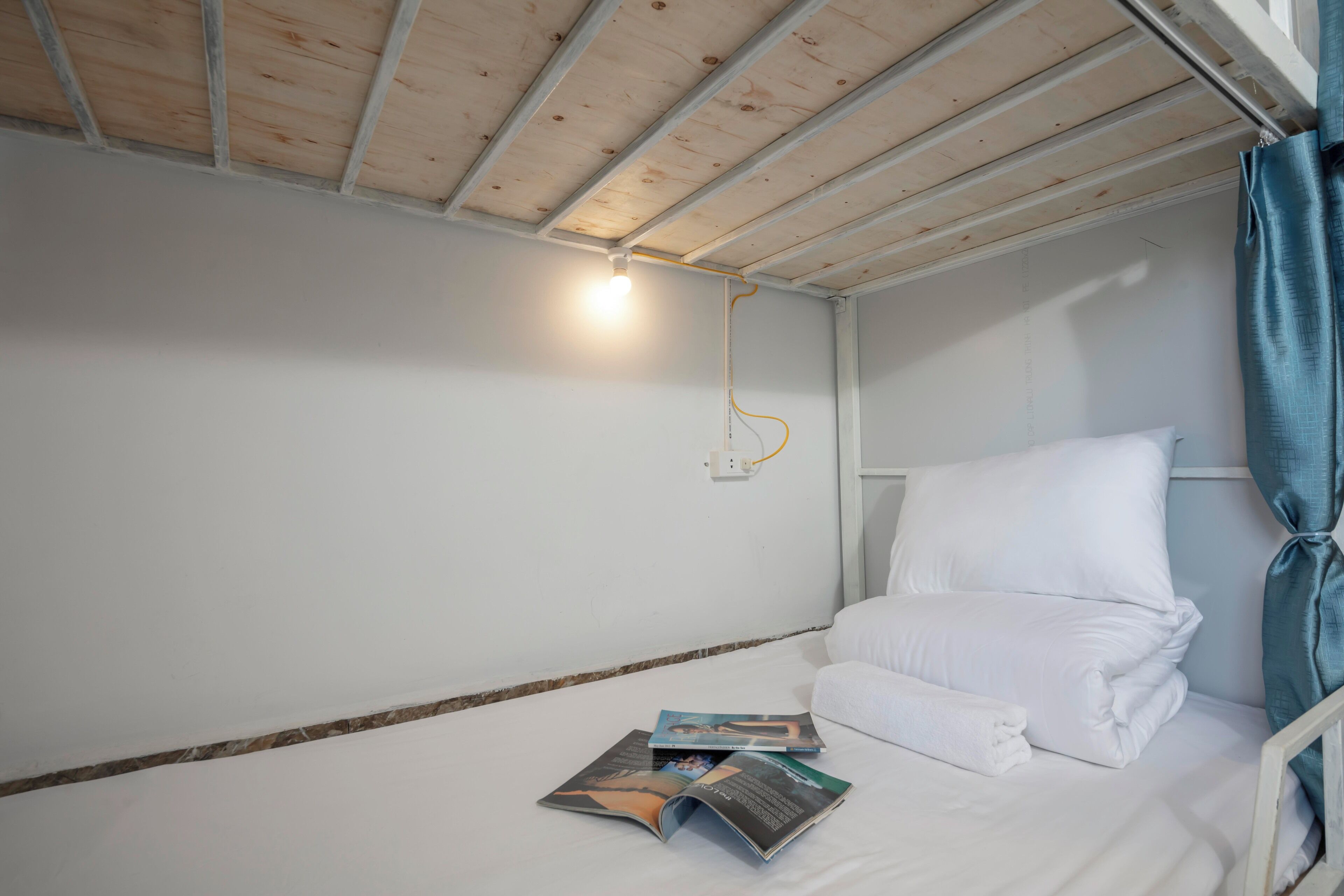 A single bed with white bedding, a blue curtain, and a light fixture on the ceiling.