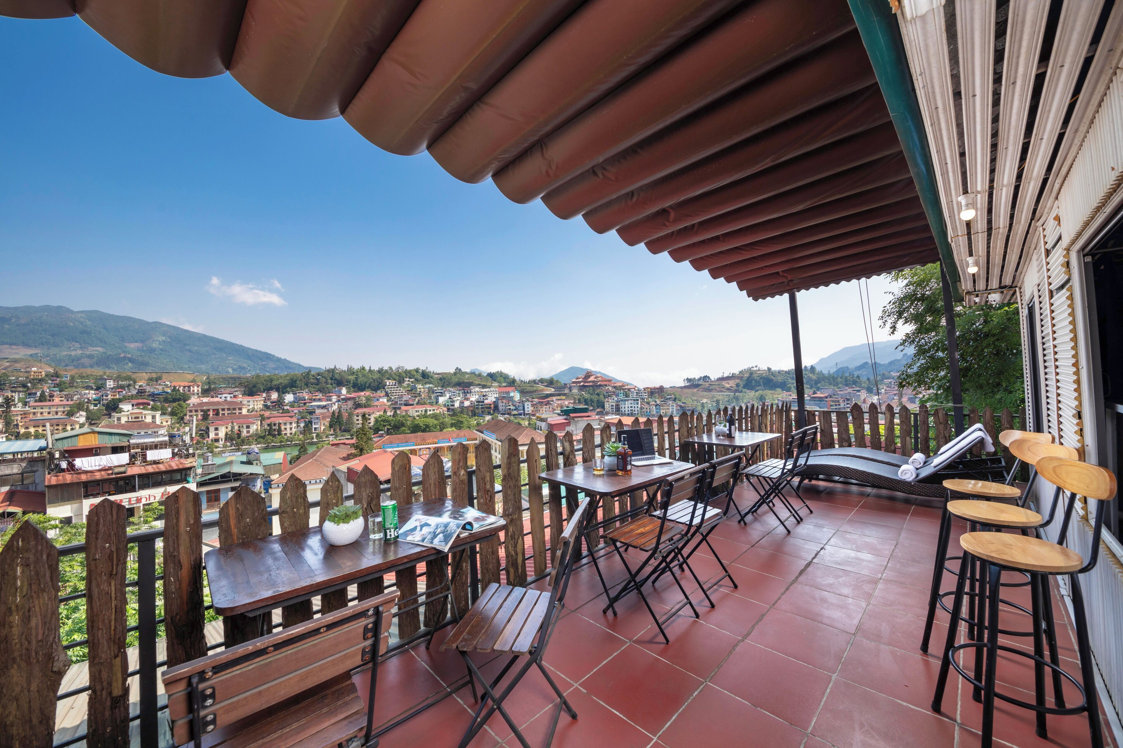 A terrace with tables and chairs, overlooking a cityscape with mountains in the distance.