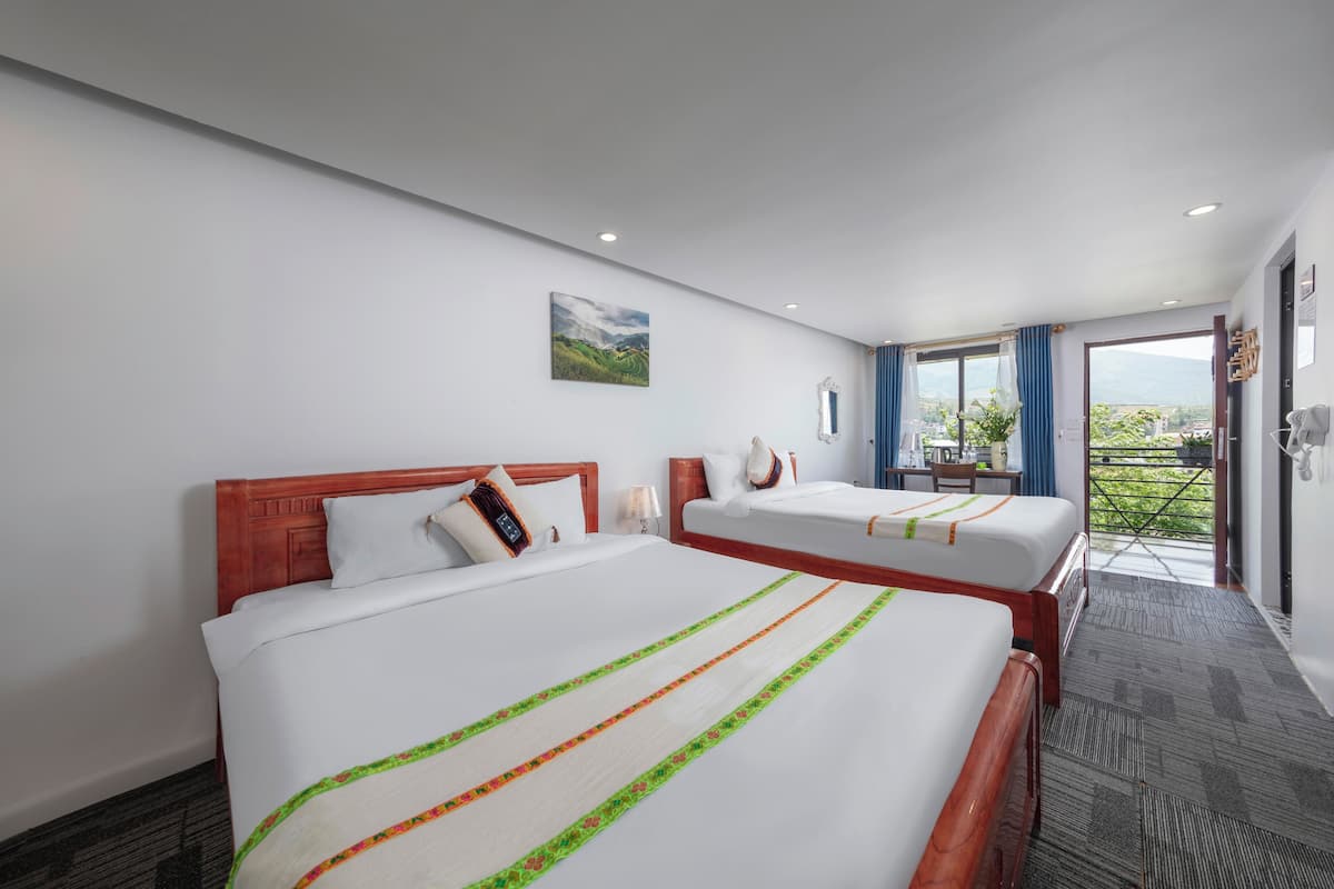 A hotel room with two beds, a painting on the wall, and a view of greenery through the window.