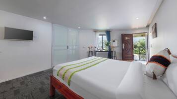 Habitación de hotel con cama, escritorio, silla, televisor, armario y puerta que da a un balcón.