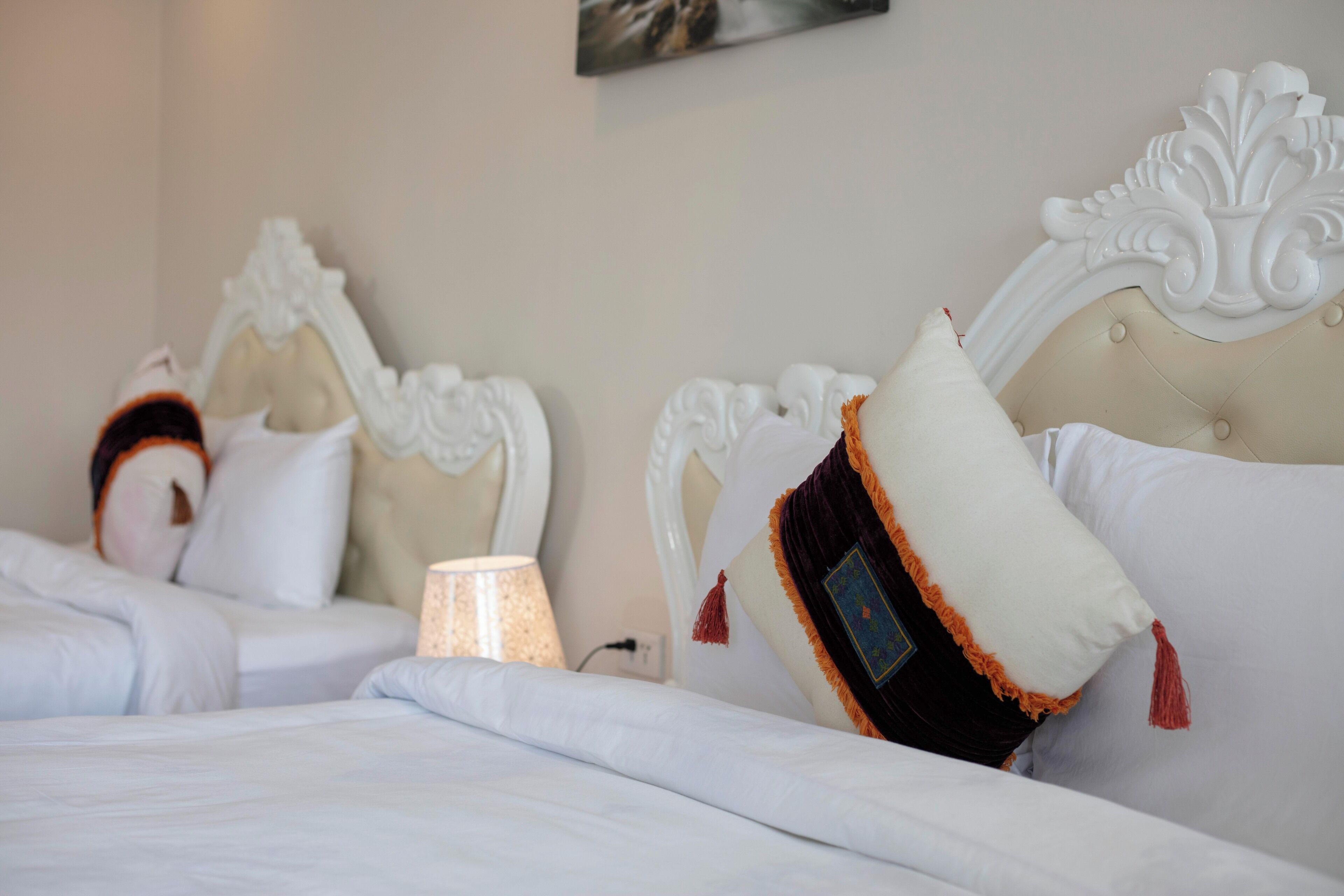 Habitación de hotel con dos camas, cada una con cabeceros decorados y varios almohadones.