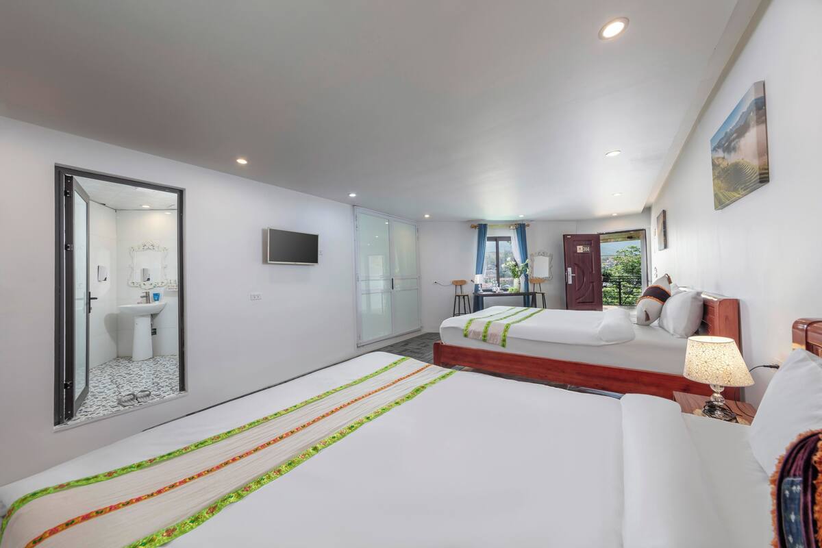 A hotel room with two beds, a bathroom, a desk, and a view of the outdoors.