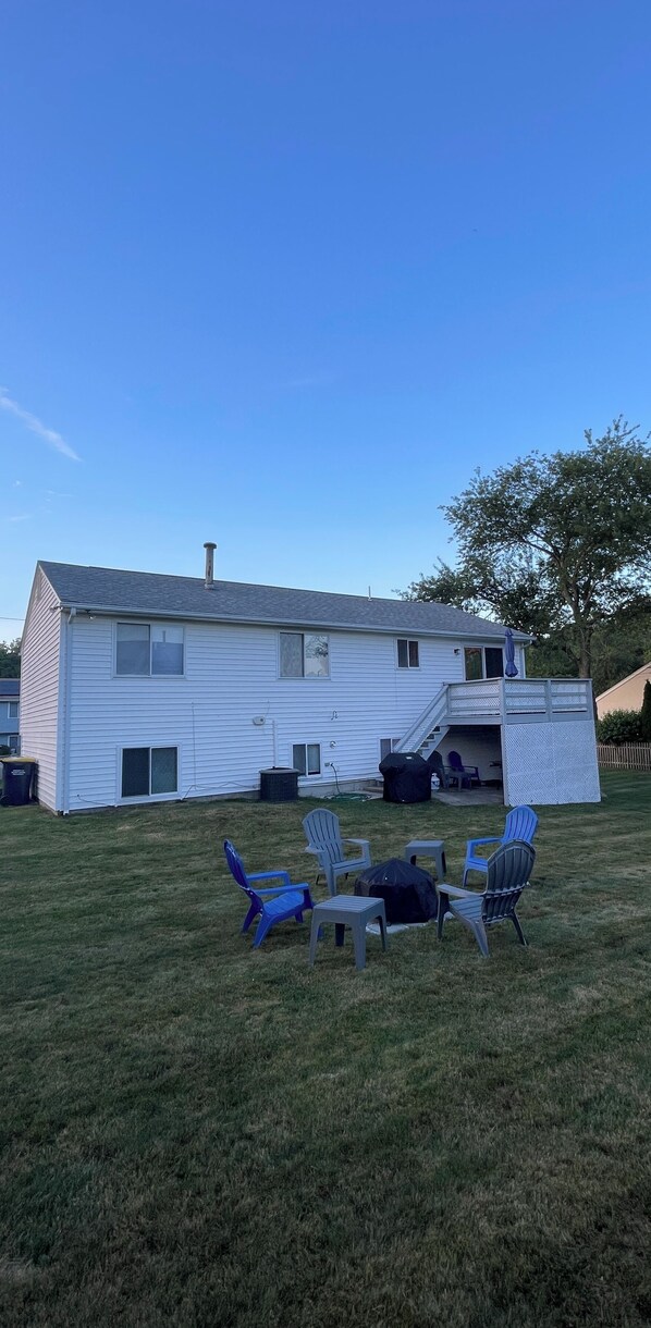 A white house with a covered patio area, outdoor seating, and a tree in the background. - Spacious Summer Rental in Bonnet Shores/Narragansett, RI. Close to area beaches. (Narragansett)