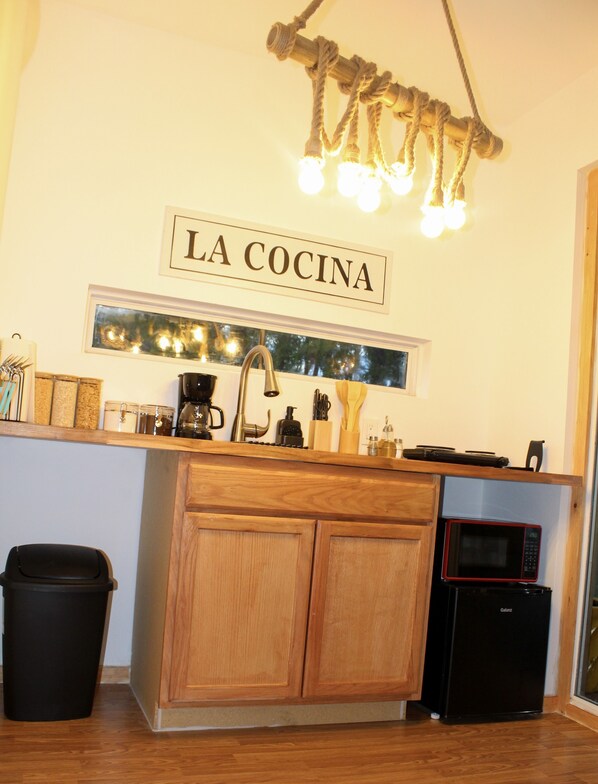 Une cuisine compacte avec des meubles en bois, un réfrigérateur noir, un four à micro-ondes et une machine à café. Une pancarte au-dessus de l’évier porte l’inscription « LA COCINA ».