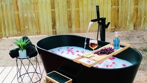 Boblebad med rosenblade, et glas vin og druer på en træbakke.