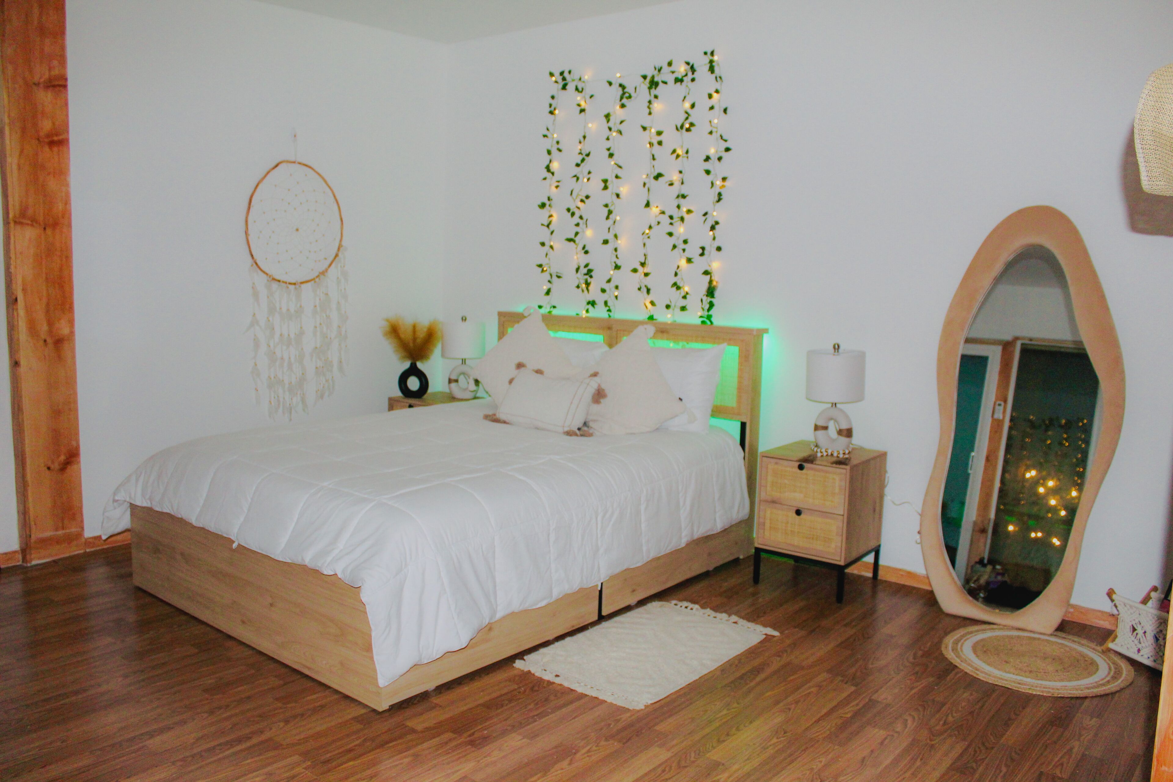 A bedroom with a wooden bed, a bedside table with a lamp, a mirror, and a wall with hanging lights.