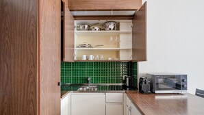 Una cocina compacta con armarios blancos, salpicadero verde y microondas integrado.