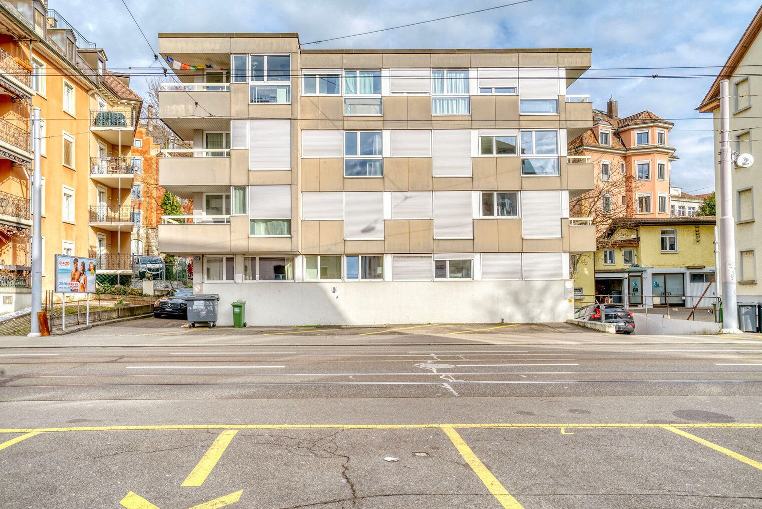Un immeuble résidentiel à plusieurs étages, doté d’une façade plate, de balcons et d’un espace de stationnement à l’avant.