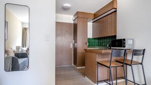 Cocina compacta con armarios de madera, un microondas y un taburete de bar.
