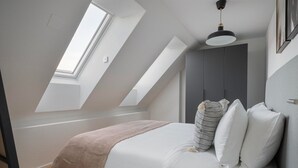 A bedroom with a sloped ceiling, skylight, bed with white bedding, and a grey wardrobe.