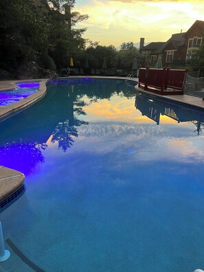 A swimming pool with a clear reflection of the sky and trees, surrounded by a fence and lounge chairs.