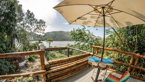 A wooden deck with a view of a lake and mountains, a bamboo fence, and a table with chairs. - Magic View Prado (Prado)