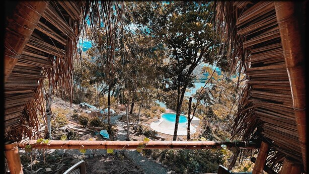 A view from a bamboo-framed structure overlooking a pool area with trees and a clear sky. - Magic View Prado (Prado)