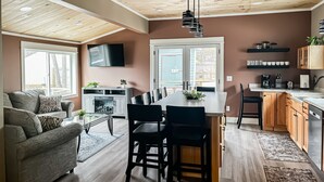 Una cocina moderna con armarios de madera, una zona de comedor con una mesa grande y una sala de estar con sofá y televisor.