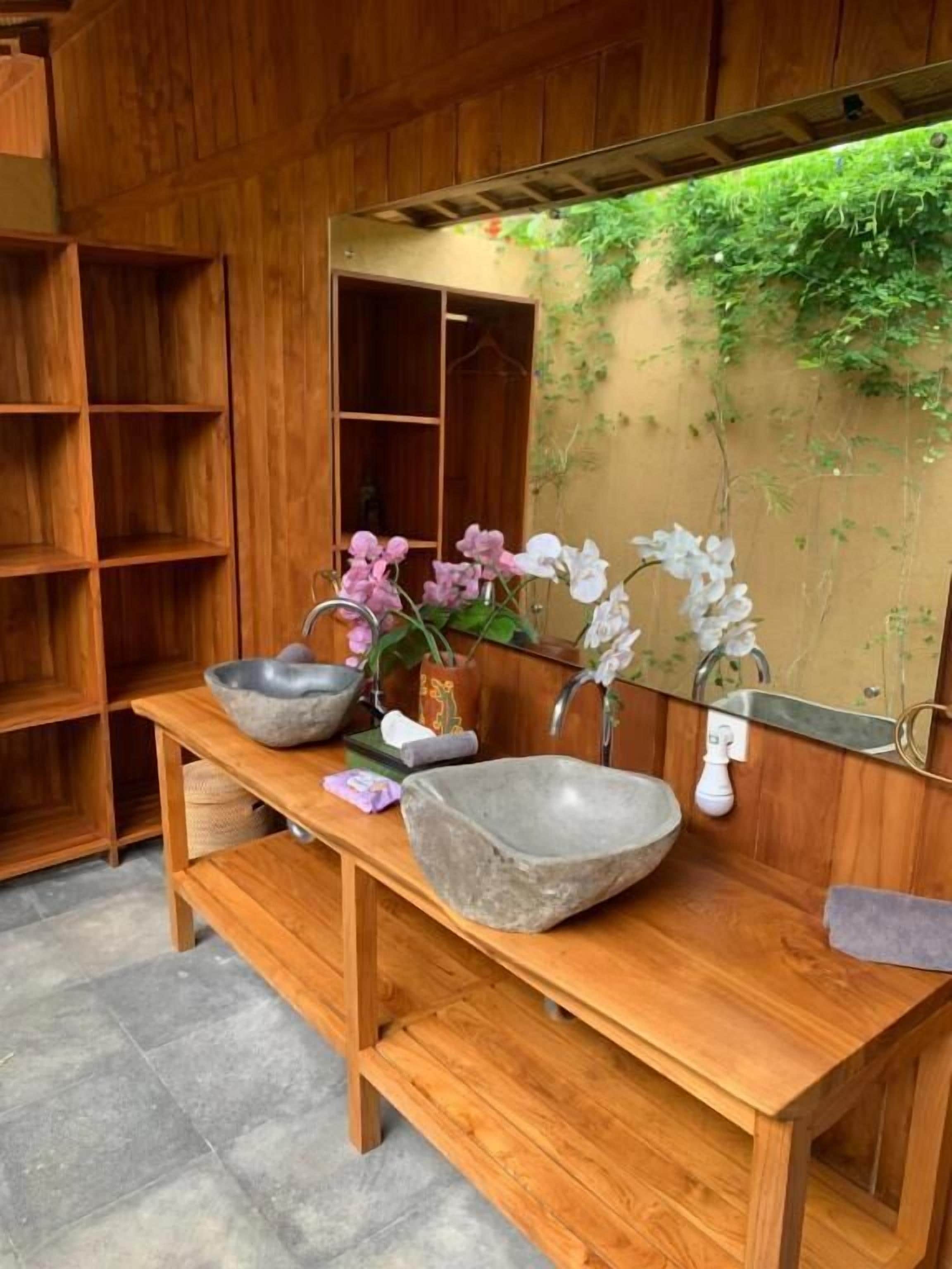 Un mobile bagno in legno con lavabo in pietra, uno specchio e uno scaffale con oggetti decorativi.