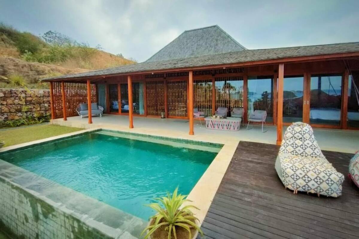 Ein Poolbereich mit Holzterrasse, Liegestühlen und einer überdachten Sitzgelegenheit mit Blick auf die Landschaft.
