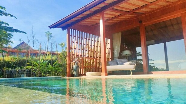 A poolside area with a wooden pergola, a lounge chair, and a view of a traditional building in the background. - Lobster Bay Resort  (Mertak)