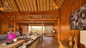 A wooden interior with a thatched roof, a sofa, a dining table, and a painting on the wall. - Lobster Bay Resort  (Mertak)