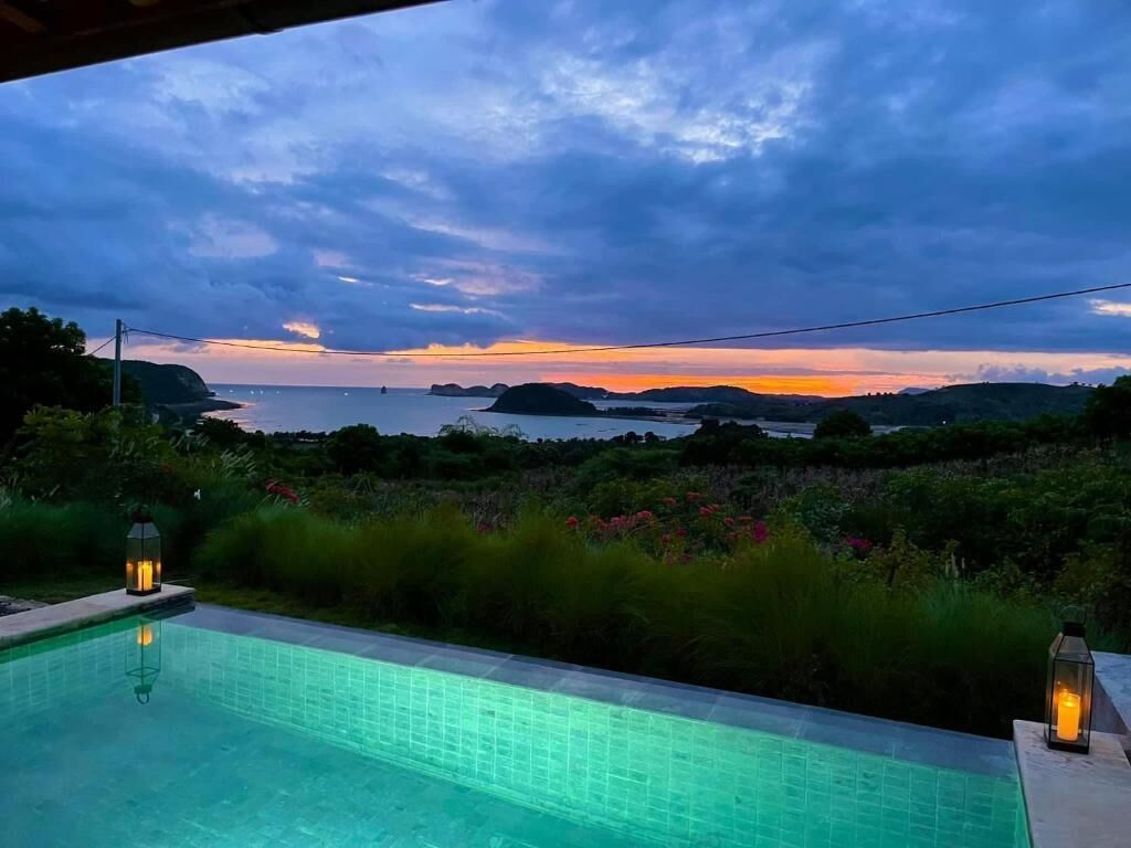 A swimming pool with a view of the sea and hills during sunset.