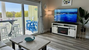 A living room with a TV, a fireplace, a balcony with blue chairs, and a large plant. - Sea View Home 6 bed 3bedroom-garage near boardwalk (Myrtle Beach)