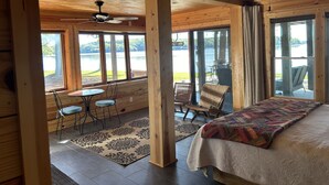 Eine Holzhütte mit einem großen Bett, einem Deckenventilator und Blick auf einen See.