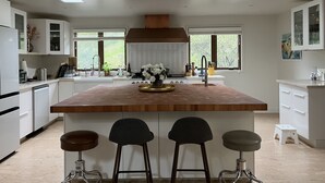 Een moderne keuken met een centraal eiland, barstoelen en uitzicht op groen.