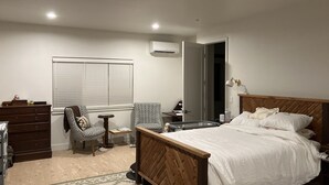 Een slaapkamer met een houten bed, een kapstok, een stoel, een klein tafeltje en een raam met zonwering.