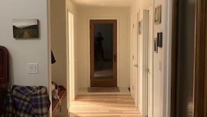 Een hal met houten vloer, een bank, een deur en een aan de muur hangend schilderij.