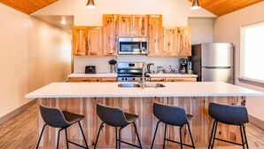 A modern kitchen with wooden cabinets, stainless steel appliances, and a central island with bar stools. - Lakeshore Lodging Luxury Suites (Homer)
