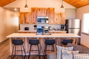 Een moderne keuken met houten kastjes, roestvrijstalen apparatuur, een centraal eiland met barkrukken, en een gezellige zithoek met gestreepte kussens.