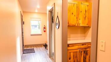 A hallway with wooden flooring, a fire extinguisher, and a door leading to a kitchen with wooden cabinets.