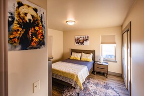Quarto com cama, mesa de cabeceira, janela com persianas e um quadro na parede.