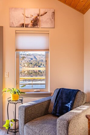 Una habitación con un ventanal grande, una silla, una pequeña mesa con una planta y obras de arte en la pared.