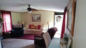 A living room with a beige sofa, a dark armchair, a small table, and a ceiling fan. - Only10 minute walk to the Inland side of Sound, 3 mile  Emerald Isle Beach,Pets (Cape Carteret)