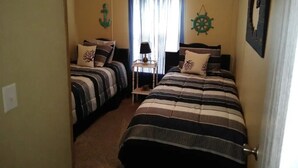 A room with two beds, each with striped bedding and decorative pillows. There is a small table with a lamp and a window with curtains. - Only10 minute walk to the Inland side of Sound, 3 mile  Emerald Isle Beach,Pets (Cape Carteret)
