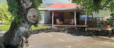 Una casa con techo rojo, un porche con sillas y un muro de piedra.