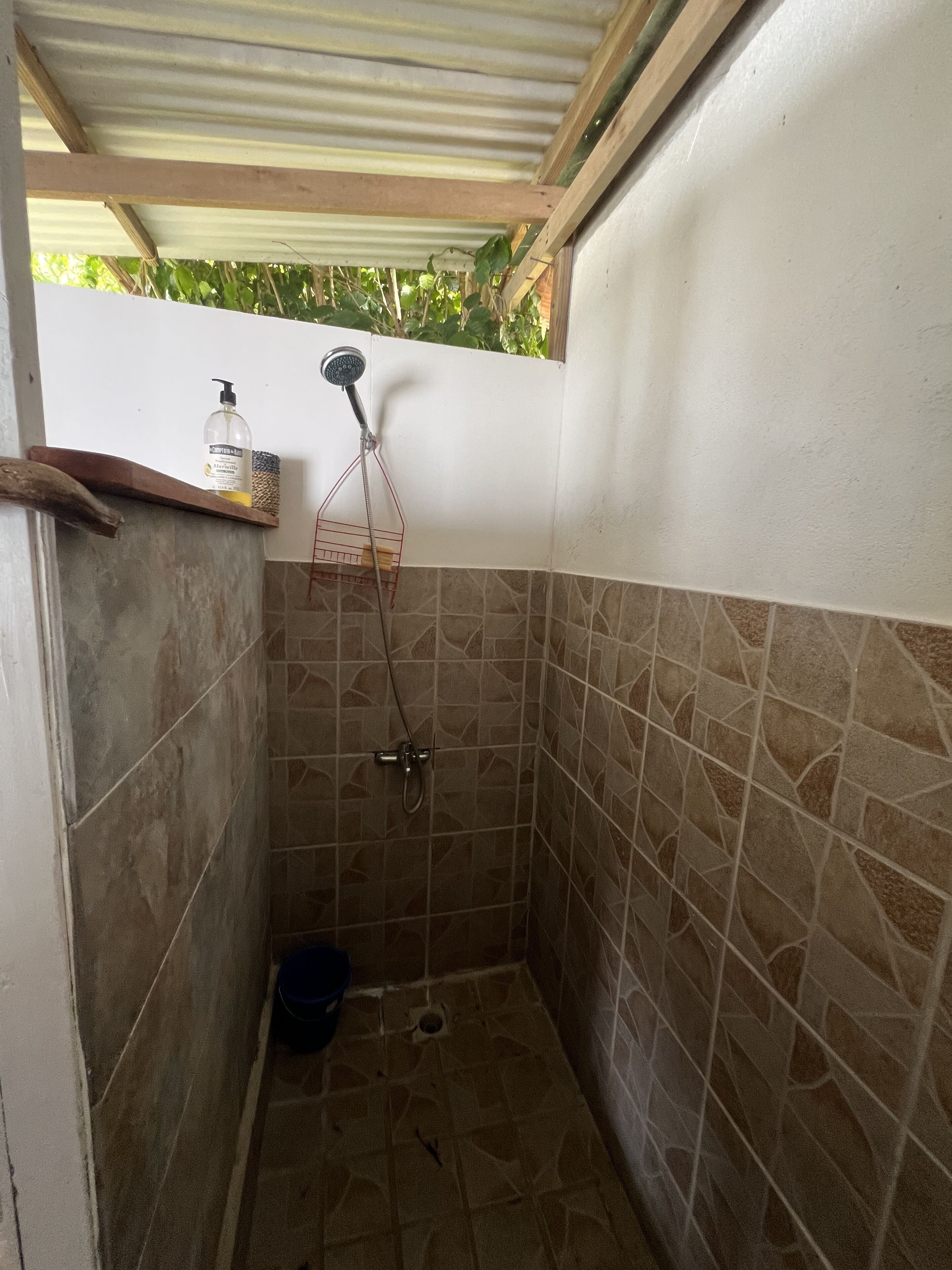Zona de bany petita amb rajola, un vàter, un dispensador de sabó i una petita repisa.