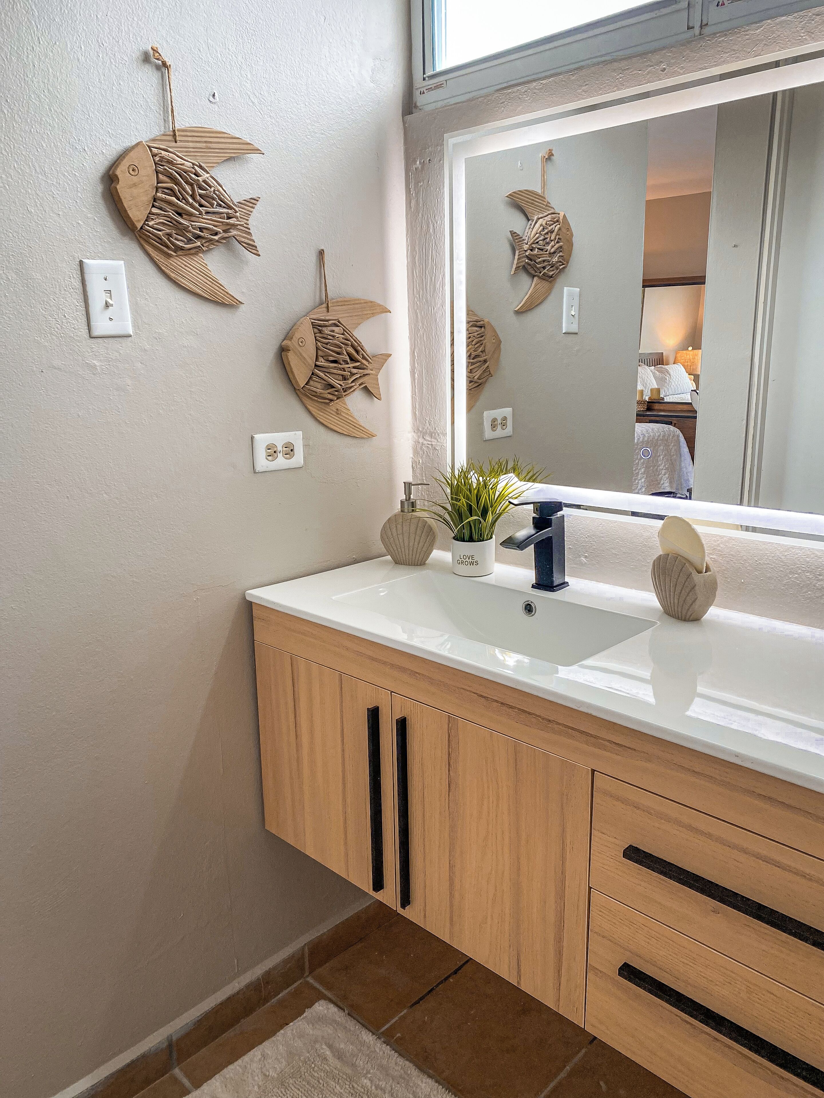 A bathroom with wooden cabinets, a white sink, and decorative fish wall art.
