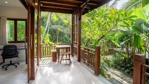 A covered balcony with a wooden table and chairs, surrounded by lush tropical plants. - D&B Mandala Villas (Ubud)