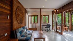 A spacious room with a wooden wall, a checkered sofa, a wooden table, a desk, and large windows offering a view of greenery. - D&B Mandala Villas (Ubud)