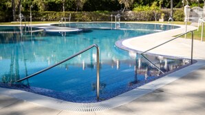 A swimming pool with a tiled edge and metal handrails, surrounded by greenery and a paved walkway. - Apartment Sleeps 4 with Sea Views (Benalmadena)