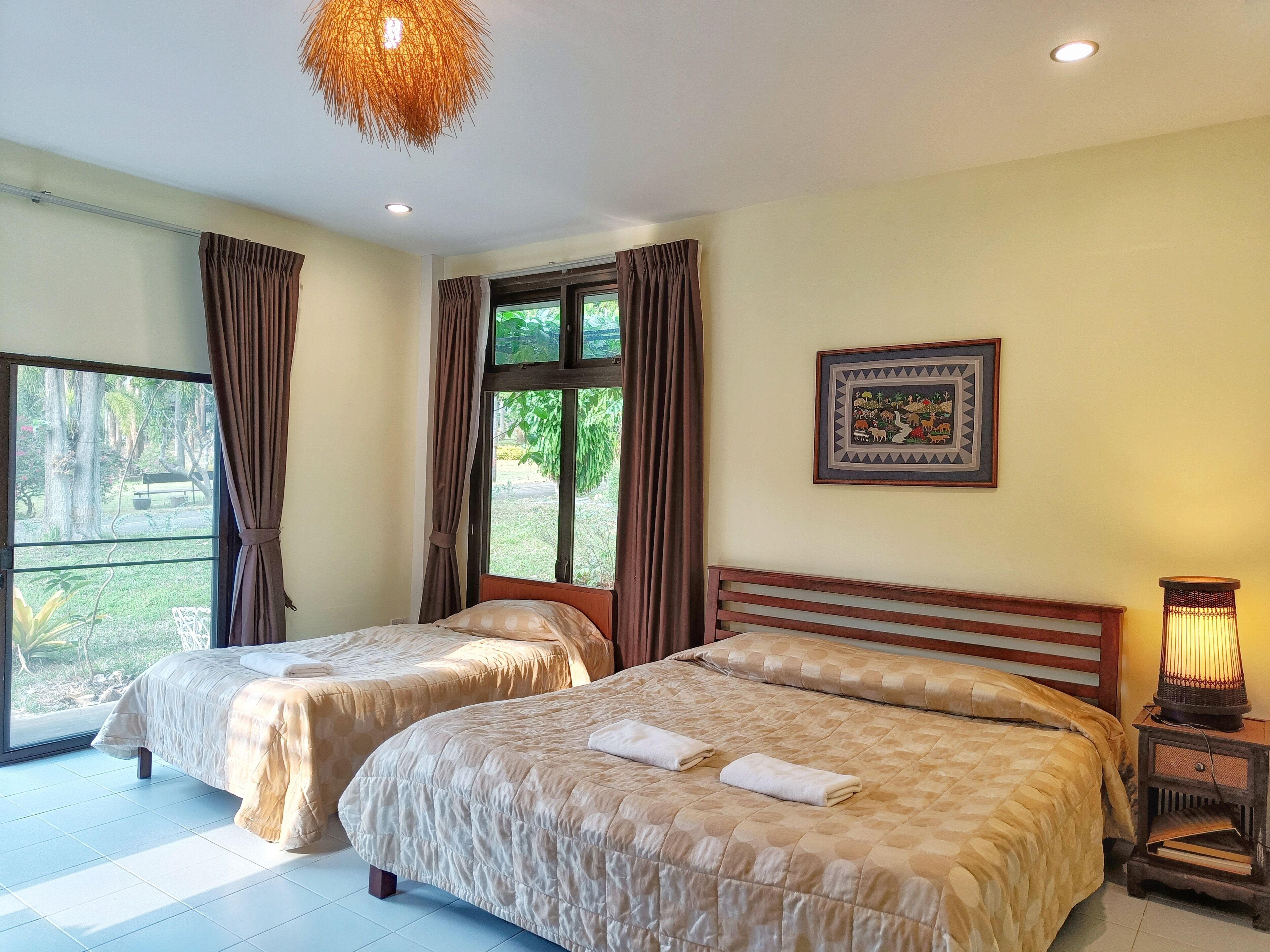A hotel room with two beds, a large window with curtains, a wall-mounted picture, and a bedside lamp.