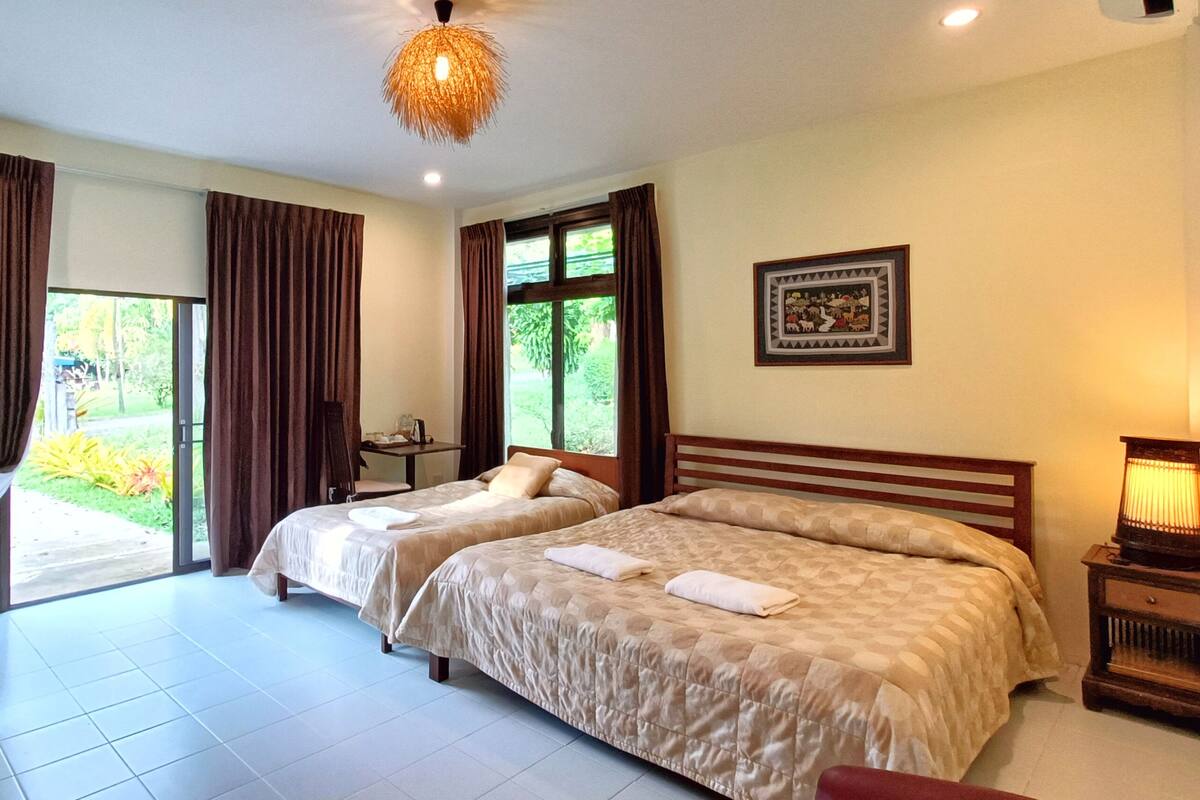 A hotel room with two beds, a desk, a chair, a lamp, and a window with curtains.