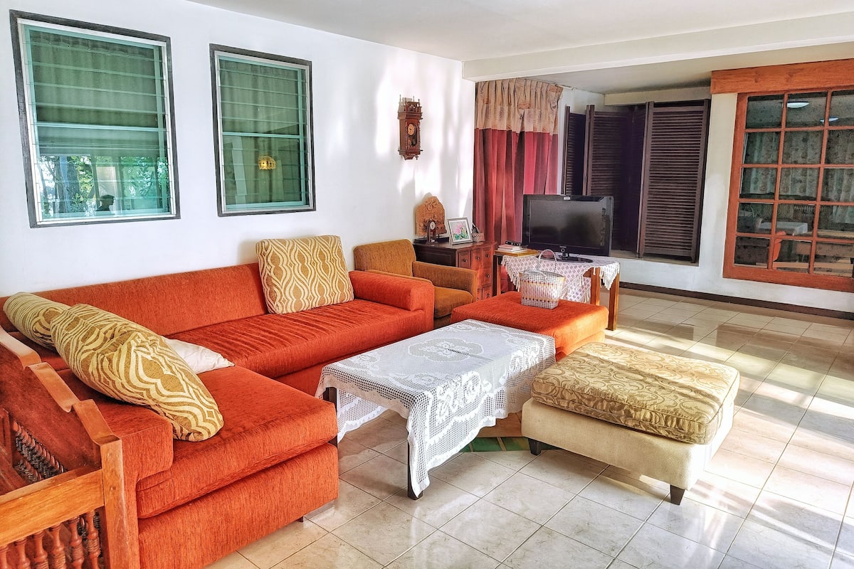 A living room with a sofa set, a television, and a table with a lace tablecloth.