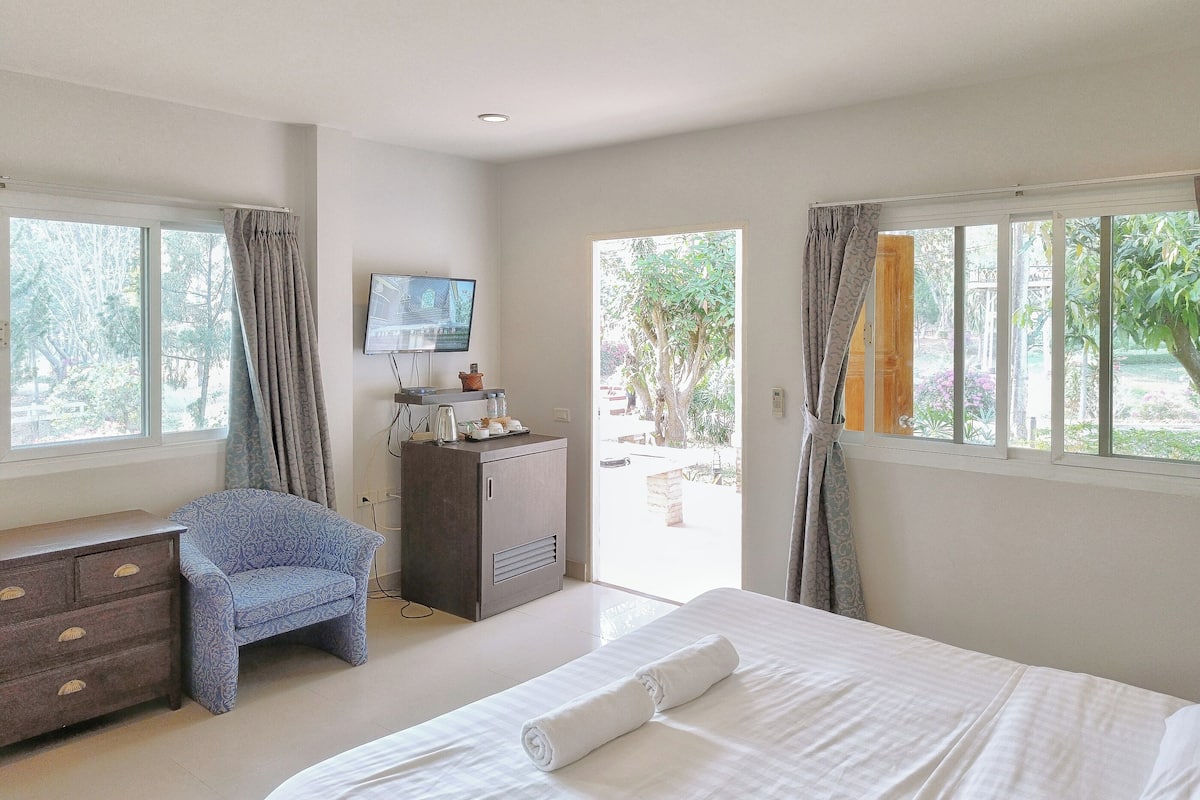A hotel room with a bed, a desk, a chair, a TV, and large windows.
