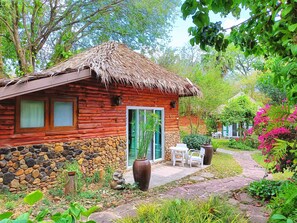 A rustic wooden cabin with a stone foundation, a thatched roof, and a stone wall. - Kong Garden Resort (Pak Chong)
