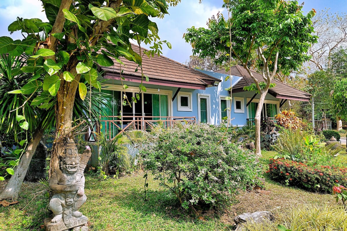 A traditional house with a tiled roof, surrounded by lush greenery and a stone statue.