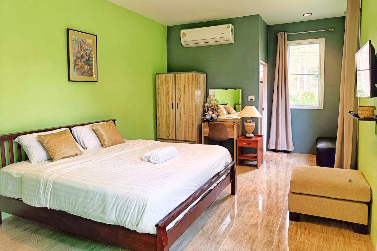 A hotel room with a bed, a desk, a chair, a wardrobe, and an air conditioning unit.