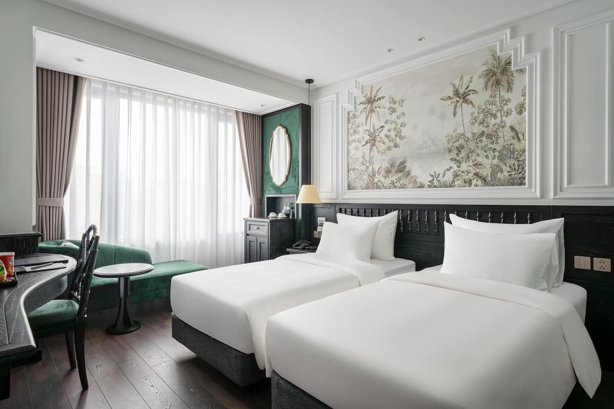 Hotellihuone, jossa on kaksi sänkyä, työpöytä, tuoli, lamppu ja suuri, kukkakuvioin koristeltu seinämaalaus.